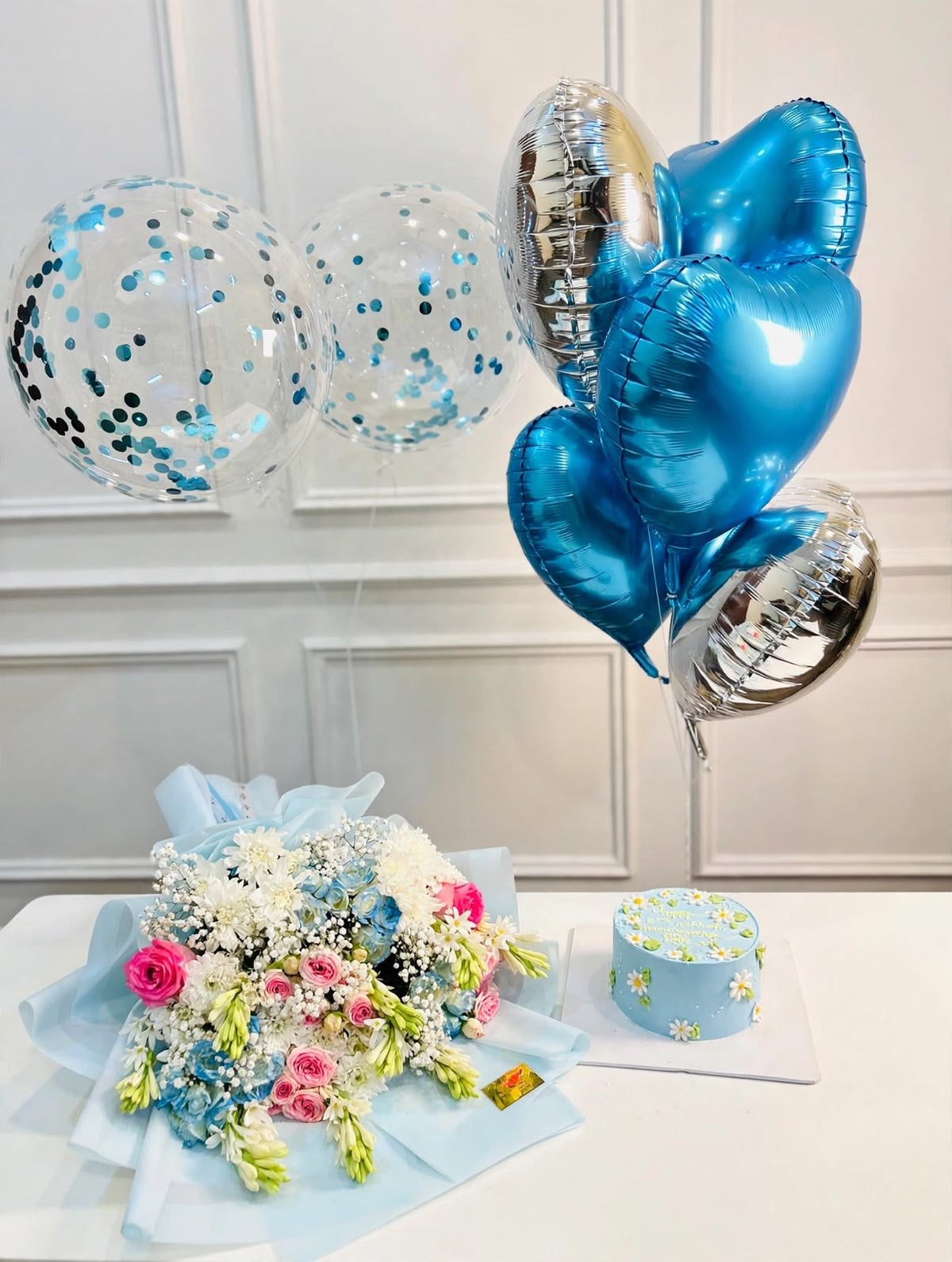 Blue birthday gift set featuring a floral cake, mixed flower bouquet in blue wrapping, and blue silver confetti balloons