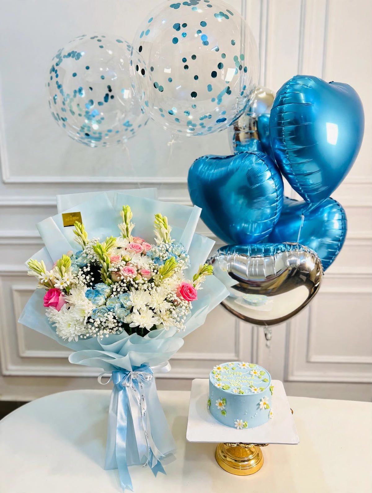 Blue birthday gift set featuring a floral cake, mixed flower bouquet in blue wrapping, and blue silver confetti balloons

