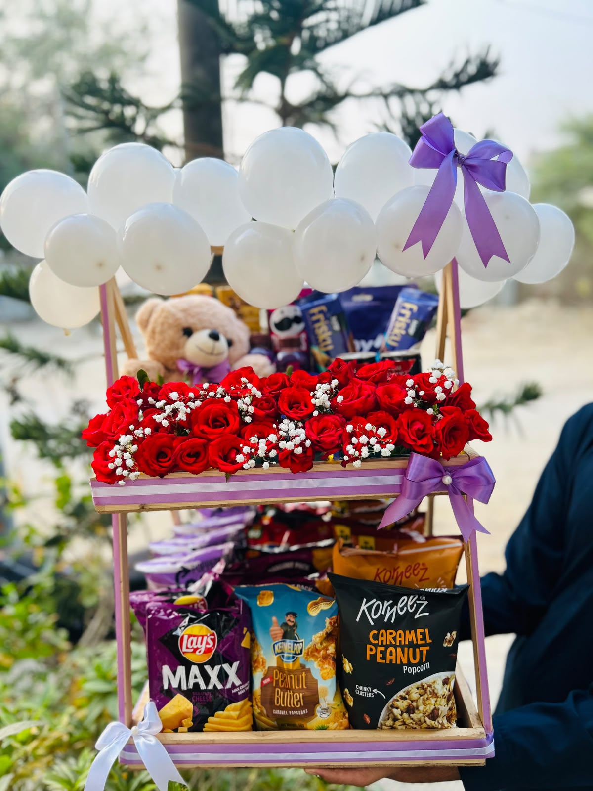 Royal Snack Surprise two-tier gift stand with red roses, teddy bear, assorted snacks, and white balloons