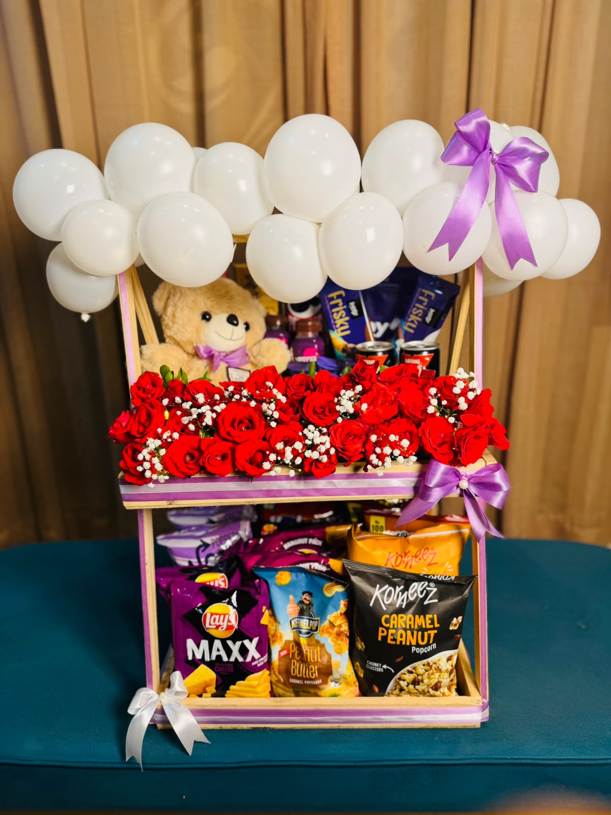 Royal Snack Surprise two-tier gift stand with red roses, teddy bear, assorted snacks, and white balloons