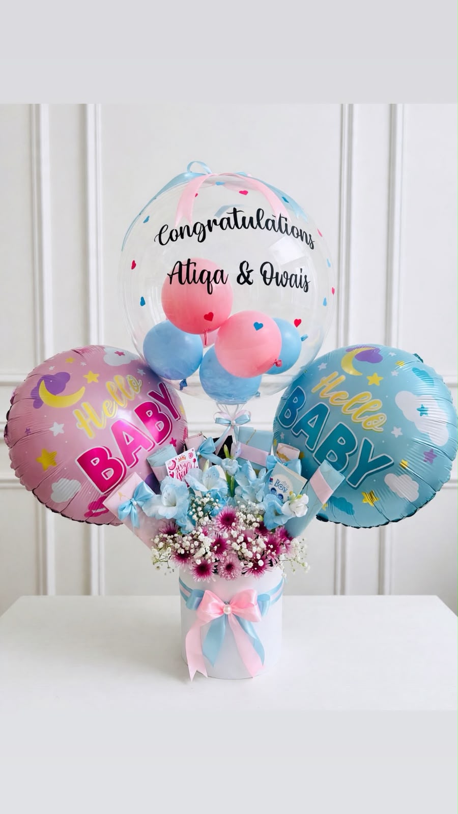 Welcome baby gift arrangement with pink and blue baby foil balloons, a clear congratulatory bubble balloon, and pastel floral bouquet